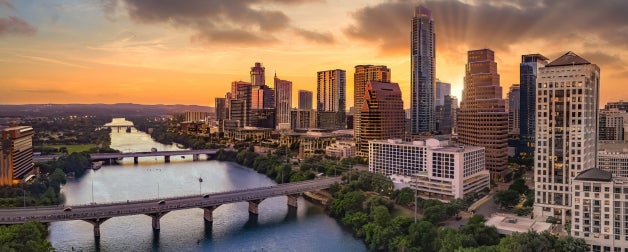 An aerial view of Lady Bird Lake and downtown Austin during a beautiful orange sunset looking north towards the skyline. You can see the Congress, South First, and Lamar Bridges.