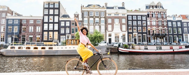 Smiling woman riding bicycle in urban street along a canal in Amsterdam, Netherlands
