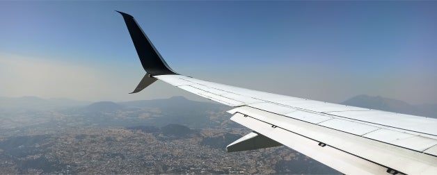 An airplane wing over an aerial landscape of a mountainous city