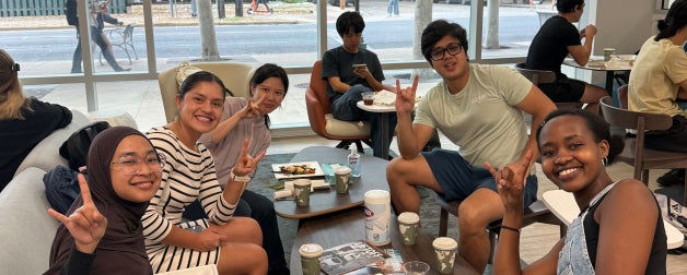 International students enjoy breakfast and fellowship in Texas Global lounge. They smile for a photo and display the hook'em sign.
