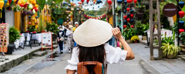 Carefree tourist woman wearing  a traditional Vietnamese hat enjoy sightseeing in the colorful Hoi An old town, Vietnam
