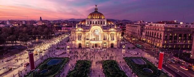 A stunning of view of the Palace of Fine Arts illuminated against a backdrop of a beautiful pink, purple, and orange sunset in the evening in Mexico City, Mexico