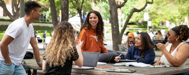 a mix of students talking together and smiling outside on the UT Austin campus
