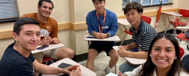 a mix of students smiling at the camera in a circle discussing language amongst each other