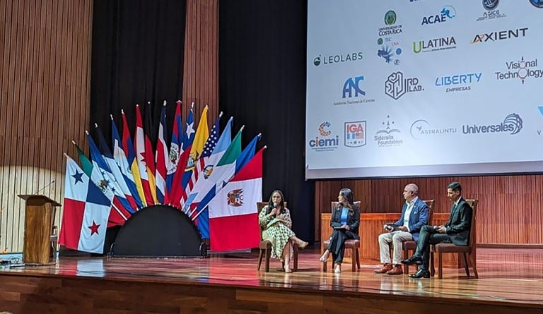 UT alum Alina Nassar speaks on a stage adorned with flags of the world