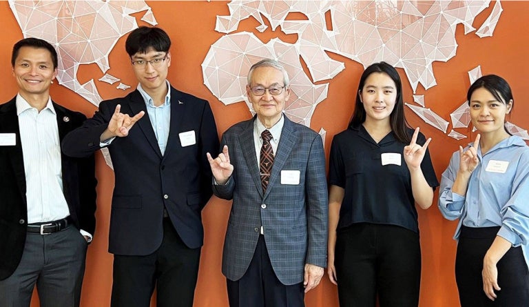 People pose in front of while and hold up "hook em" sign. 