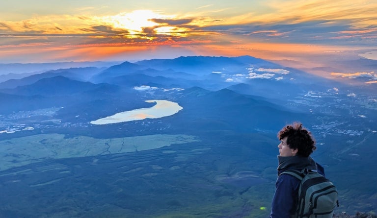UT student stands in front of a blue mountain and orange sunrise