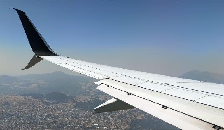 An airplane wing over an aerial landscape of a mountainous city