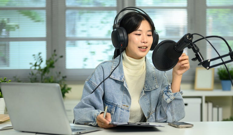 A woman with headphones speaks into a podcasting microphone.
