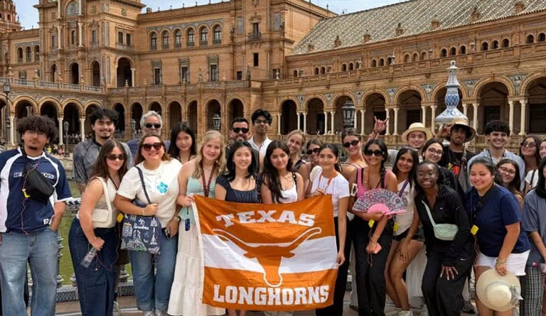 Students hold up a "Texas Longhorns" Flag in front of a Castle.