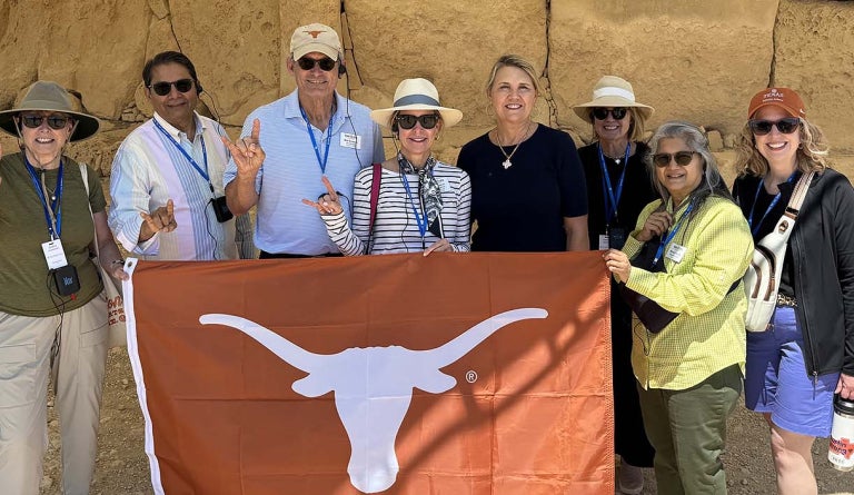 A group of travelers hold a "Longhorns" flag in front of ruins.