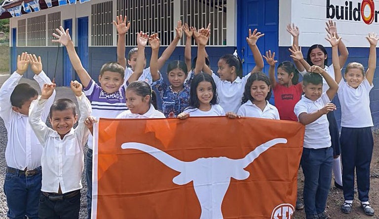 Children in Nicaragua hold up a "Texas Longhorns" flag in front of a school.