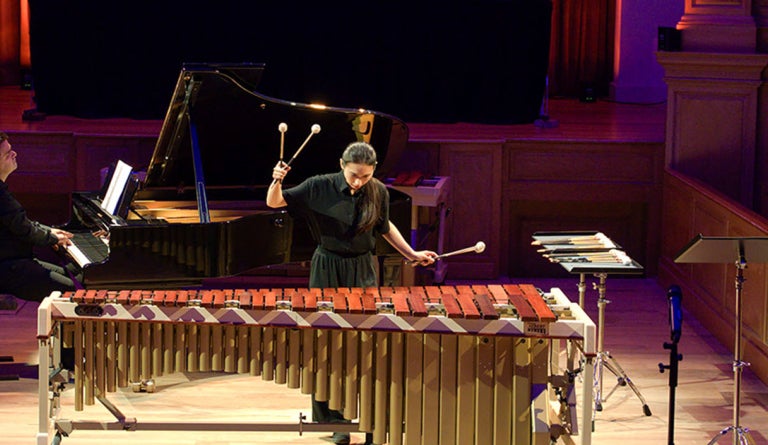 A woman plays a marimba in a music performance hall.