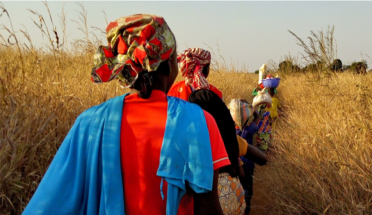 Photo of African women dressed in traditional wardrobe, walking through a field 