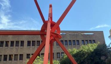 large red metal sculpture in front of buildings and trees during daytime