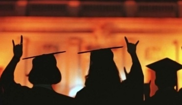 silhouettes of students in graduation caps and gowns on orange and yellow background 