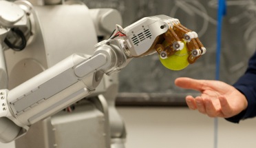 A robotic arm transfers a tennis ball to a human hand