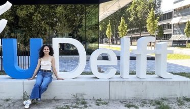 Student Jackie Villalobos sits in front of the sign for TU Delft