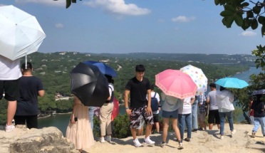 International students hold umbrellas, looking out over Mt. Bonnell in Austin