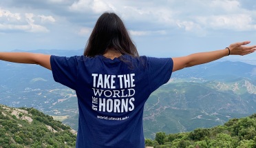 A UT student stands before a stunning landscape with arms outstretched