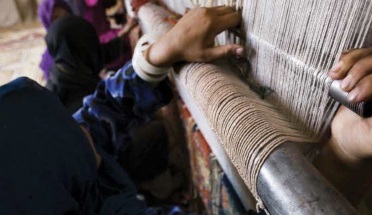 A weaver's hands on a traditional rug loom