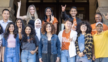 College students of many races smile and throw the UTexas 'Hook 'em Horns" symbol