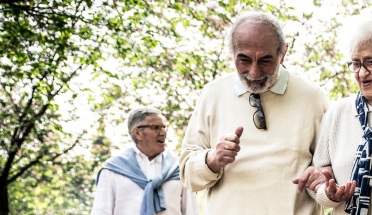 Older Latinx couple walks close together under trees