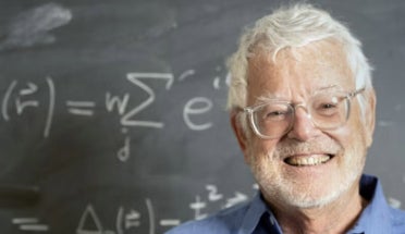 UT physicist Allan McDonald smiles by a blackboard bearing equations