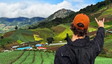 Back of male UT student showing "Hook 'em Horns" to scenic countryside