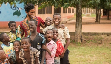A Peace Corps volunteer laughs with several children