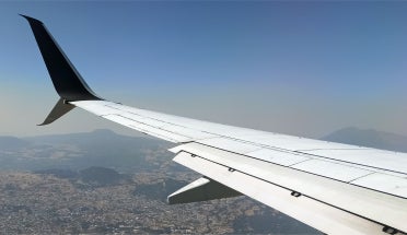 An airplane wing over an aerial landscape of a mountainous city