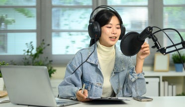 A woman with headphones speaks into a podcasting microphone.