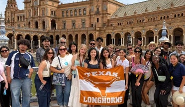 Students hold up a "Texas Longhorns" Flag in front of a Castle.