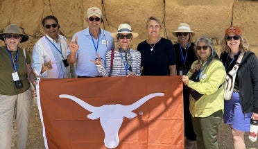 A group of travelers hold a "Longhorns" flag in front of ruins.