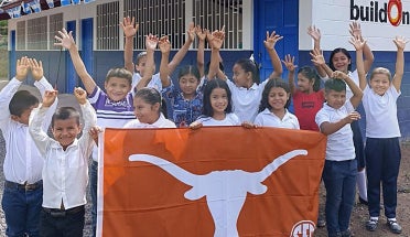Children in Nicaragua hold up a "Texas Longhorns" flag in front of a school.