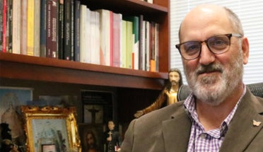 A professor poses for a portrait in his office, in front of a bookshelf.