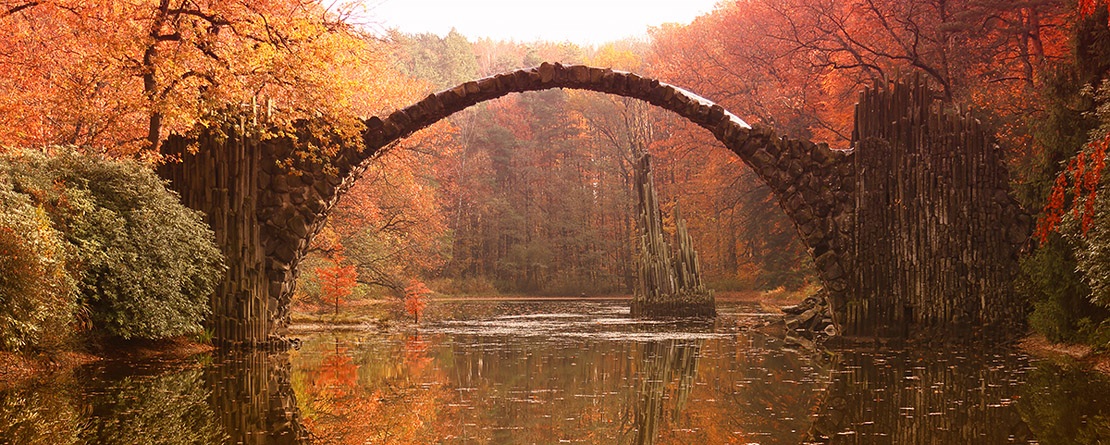 a beautiful old archway traverses water surrounded by fall colors