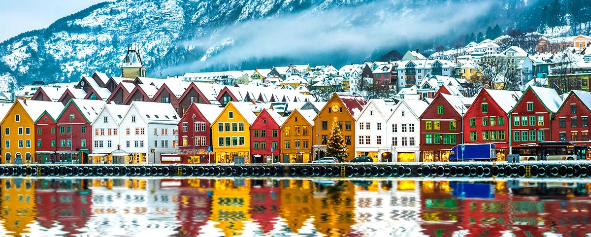 Colorful row homes topped with snow are beautifully reflected in the water, backdropped by snow covered mountains