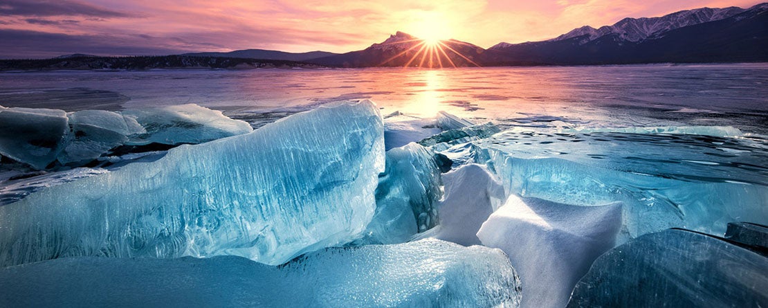 Vivid blue ice in the foreground backdropped by a sunset on Abraham Lake, Alberta in the Canadian Rockies
