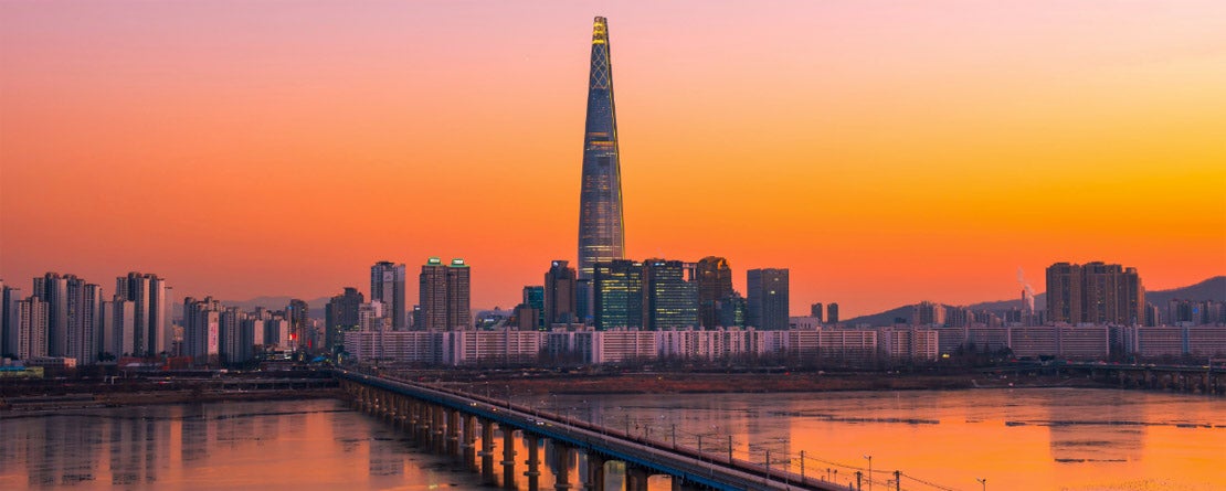 Looking down the Han River bridge at city skyline of Seoul, South Korea backdropped by a beautiful pink, orange, and yellow sunset