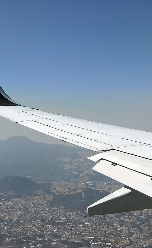 An airplane wing over an aerial landscape of a mountainous city
