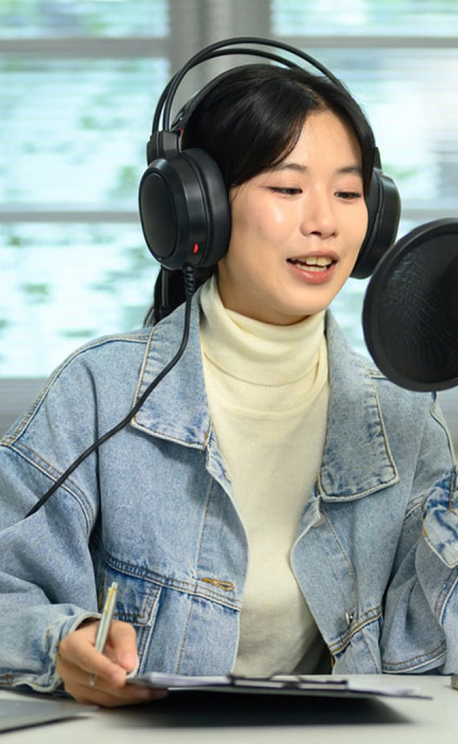 A woman with headphones speaks into a podcasting microphone.