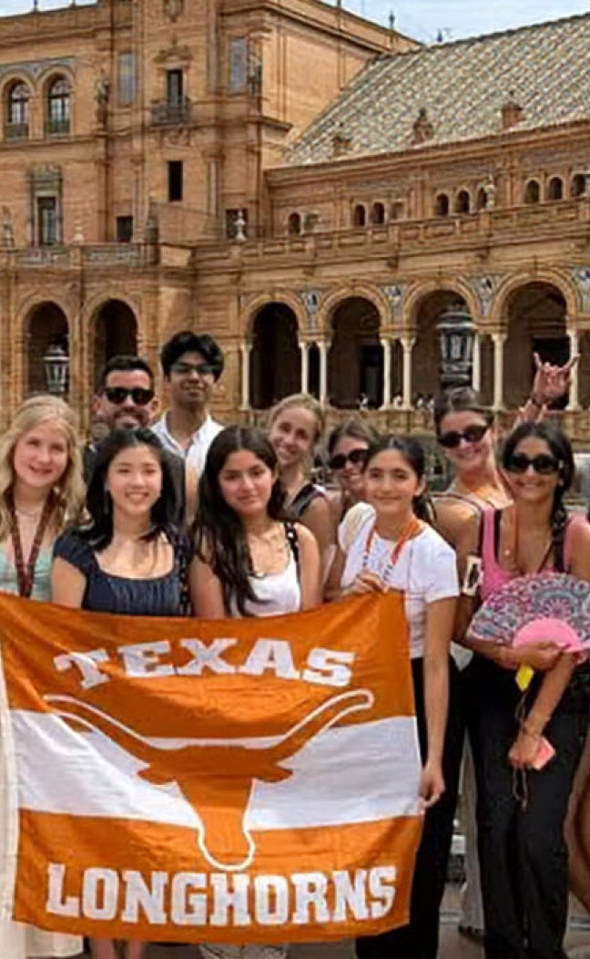 Students hold up a "Texas Longhorns" Flag in front of a Castle.