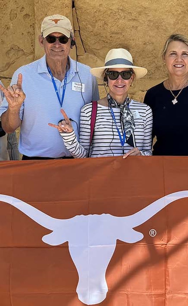 A group of travelers hold a "Longhorns" flag in front of ruins.