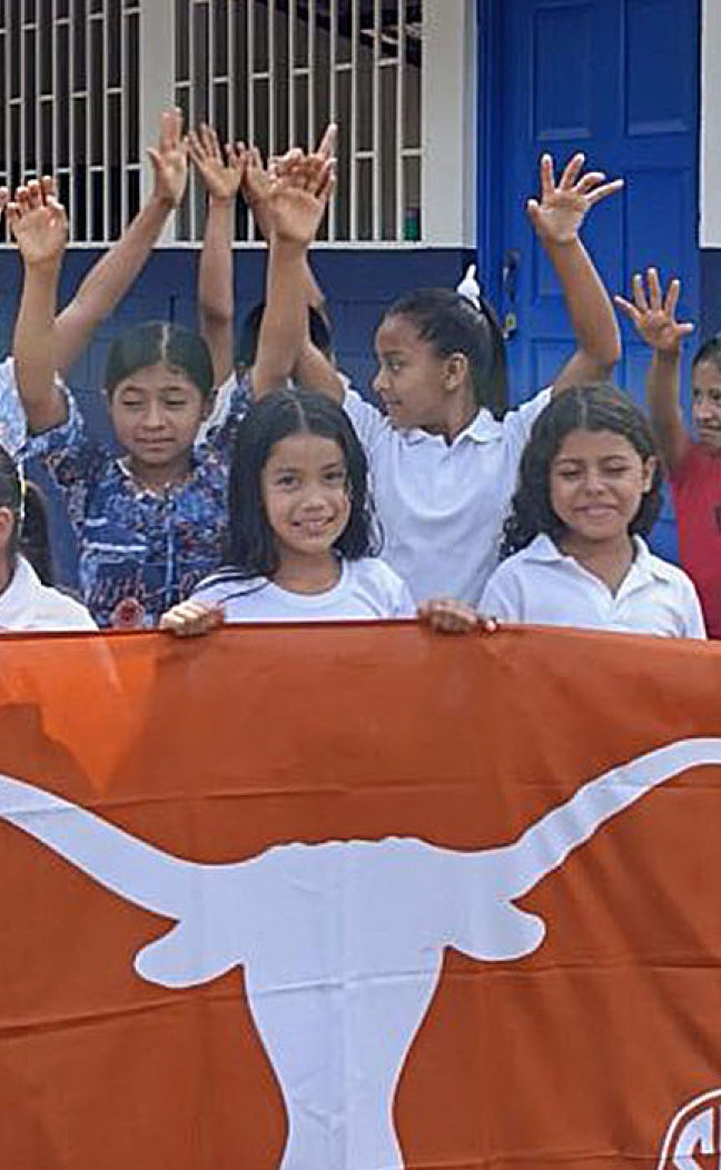 Children in Nicaragua hold up a "Texas Longhorns" flag in front of a school.