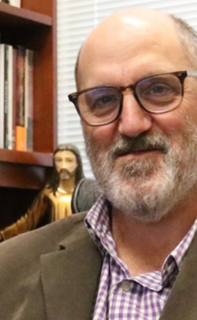 A professor poses for a portrait in his office, in front of a bookshelf.