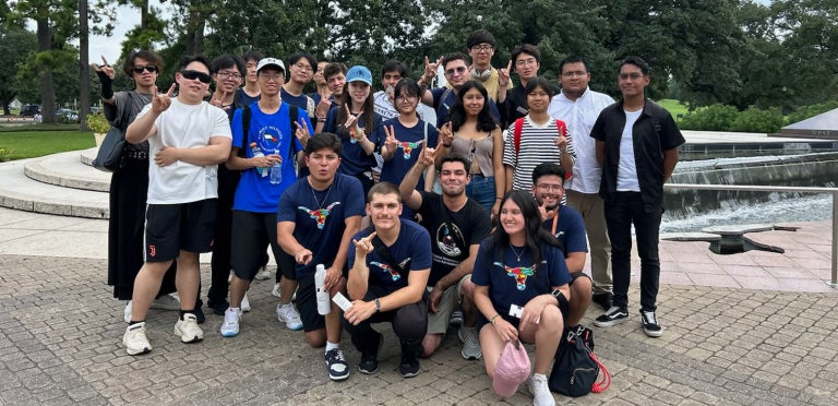 An ELC Global Summer Institute group poses while displaying the hook'em sign