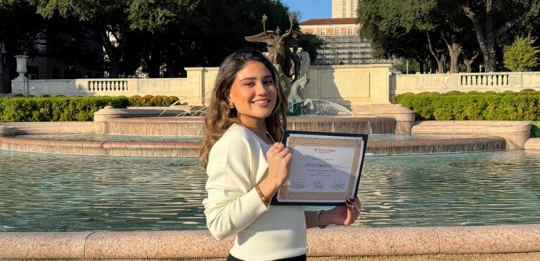 Camila shows off her diploma in front of Littlefield fountain with the UT Tower in view