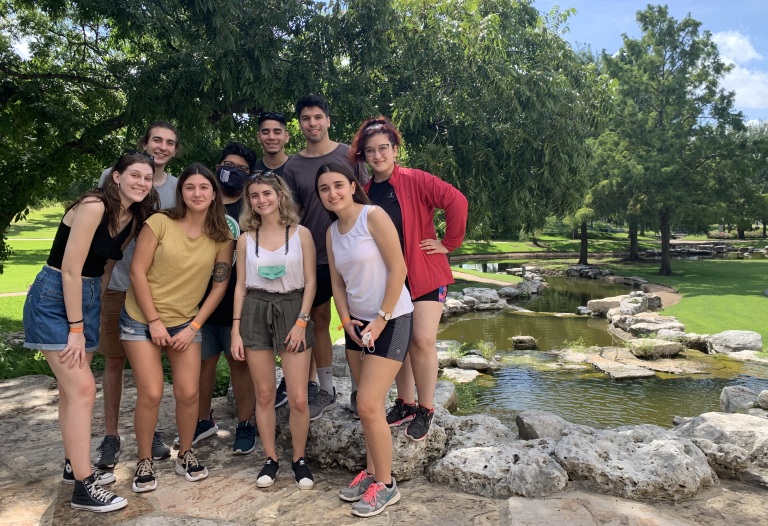 Group of smiling students pose in park with creek in background