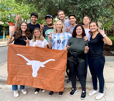 Group of smiling students hold the Longhorn flag and throw up the Hook 'Em sign